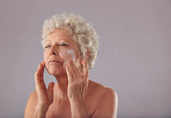 Mature caucasian woman applying anti-wrinkle face cream.