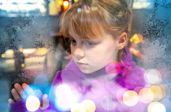 Little blond girl looks through frozen shop window glass