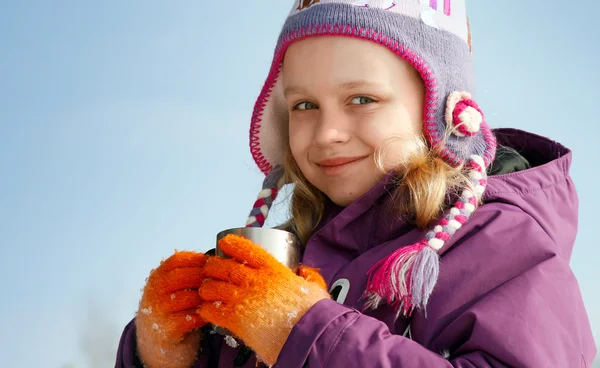 Smiling little blond girl in cold season wears winter outwear with metal cup