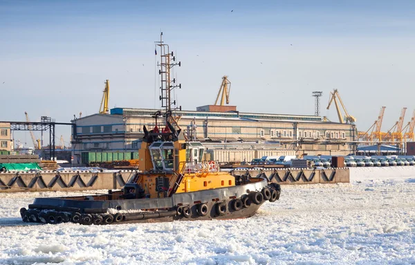 Small tug boat goes on icy channel in harbor of St.Petersburg cargo port