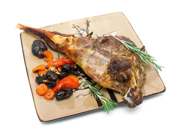 Baked leg of lamb with carrots, prunes and rosemary on a plate o
