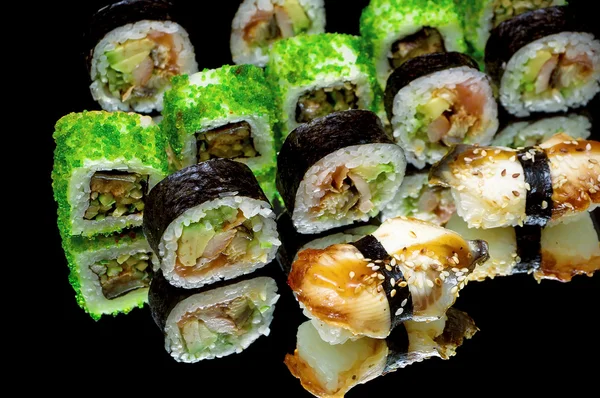 Sushi and rolls on a black background with mirror reflection