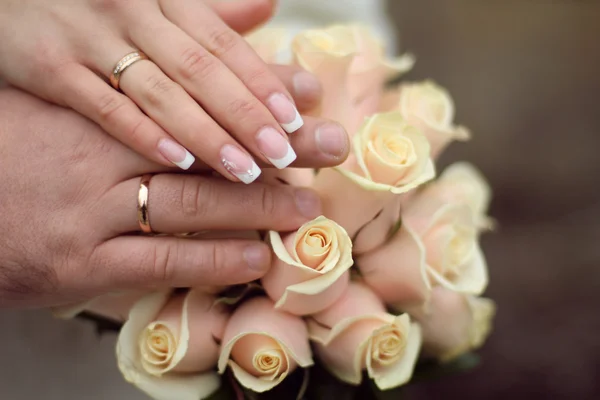 Wedding rings and Hands on roses bouquet