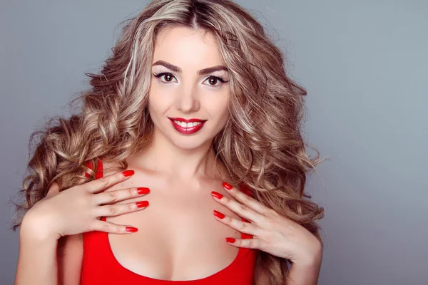 Beautiful woman with wavy hair and red manicure nails on grey ba