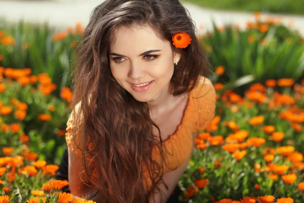 Beautiful smiling woman with long healthy hair over flowers, out