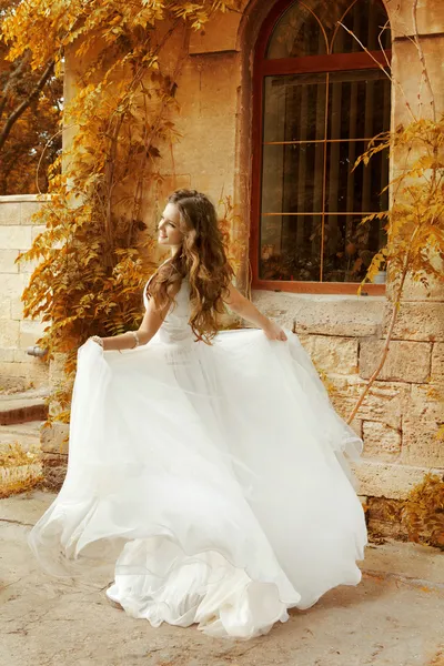 Beautiful bride woman in white wedding dress running at autumn p