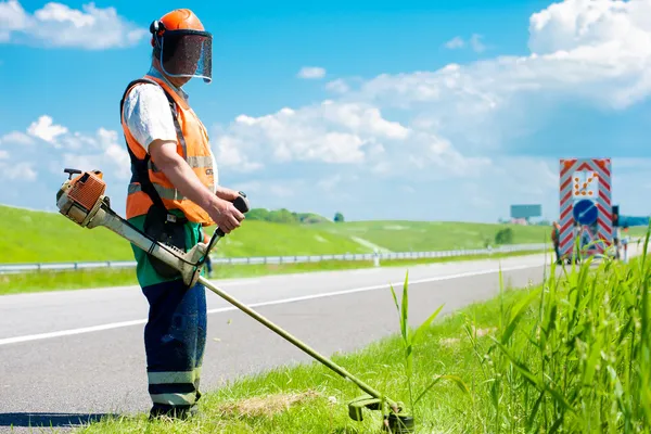 Road landscaper cutting grass using string lawn trimmer