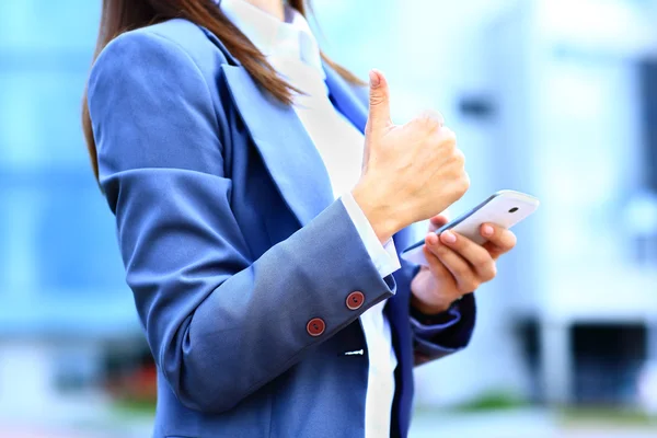 Pretty young business woman using mobile phone outdoor and ok sign