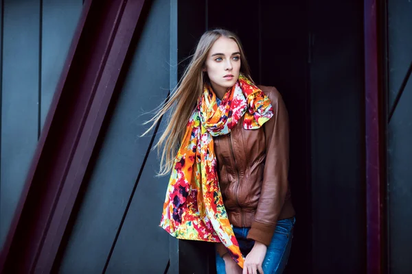 Beautiful fashion woman wearing leather coat and scarf posing against modern wall