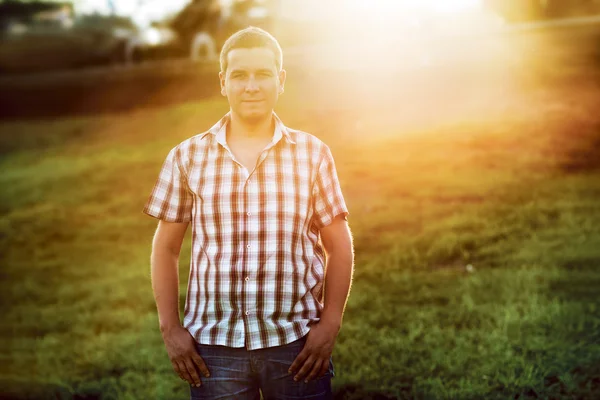Young casual man standing on the green grass in the park on the sunset