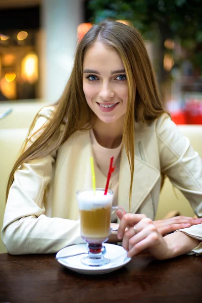 Beautiful smiling woman drinking coffee cocktail in cafe
