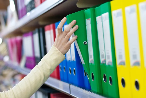 Girl\'s hand taking big folder from the shelves with office files.