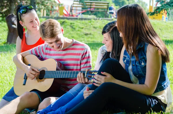 Four happy teen friends playing guitar in green summer park