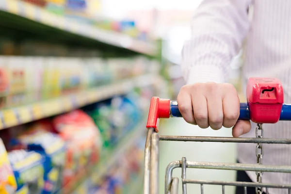 Closeup on man or woman in shop with shopping trolley or cart closeup on hand on the supermarket shelf background
