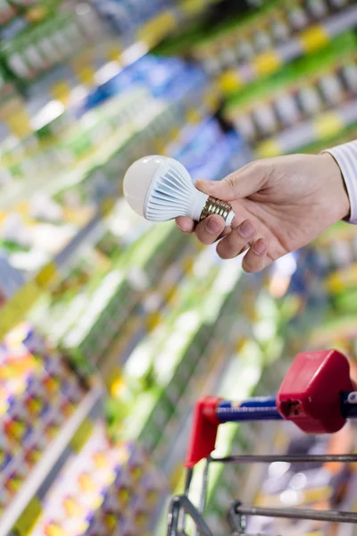 Choosing energy efficient lighting: closeup on male or female hand holding or selecting LED diode light bulb lamp in DIY department store with product display shelfs shop on the background
