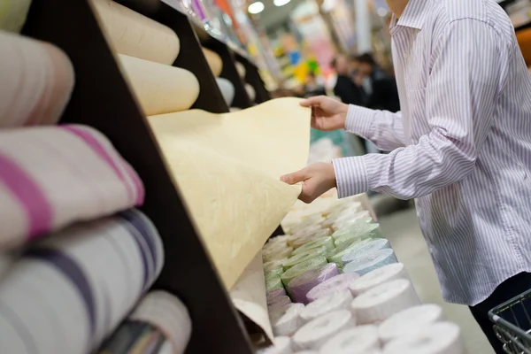 Man holding rolls of wallpaper in a supermarket