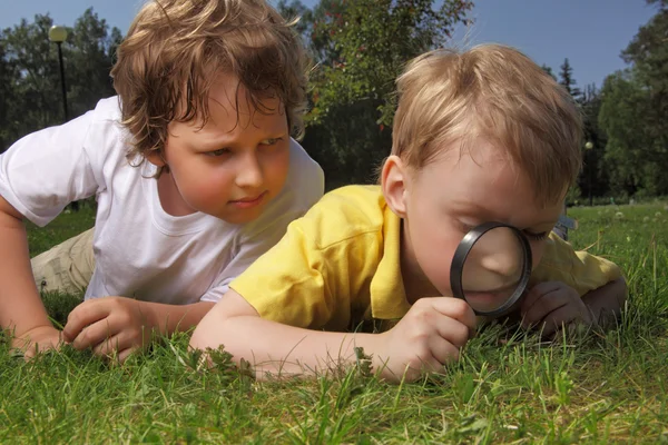 Two boys with magnifying glass outdoors