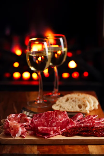 Platter of serrano jamon Cured Meat with cozy fireplace and wine