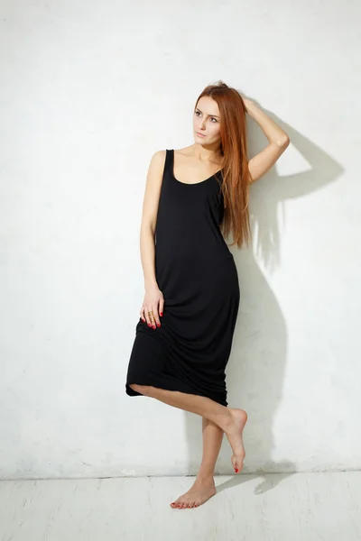 Skinny girl with long legs in black dress standing on a white fl