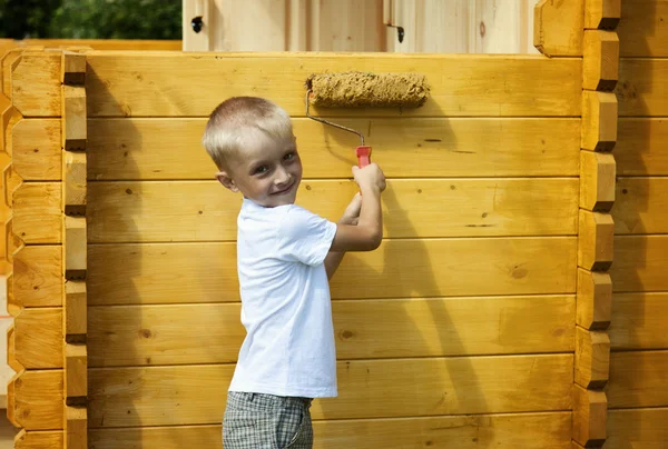 Cute little blond boy painting orange wall