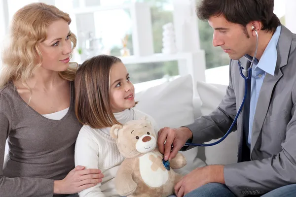 Sick little girl holding teddy bear while doctor check her