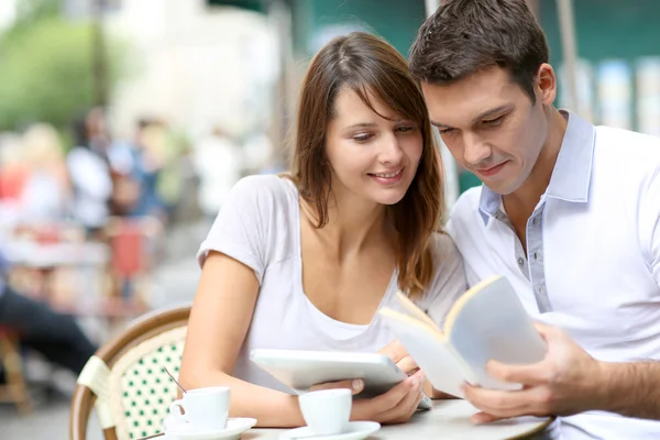 Couple on a coffee shop terrace reading tourist book