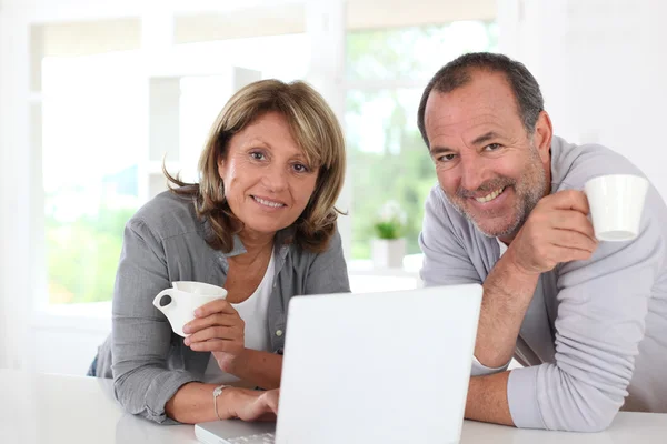 Senior couple drinking coffee in front of laptop computer