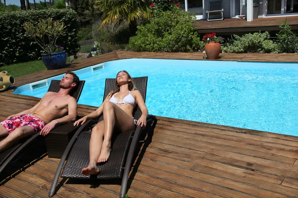 Couple in long chairs by swimming pool