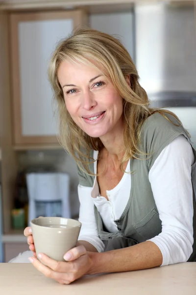 Attractive adult woman holding mug in home kitchen