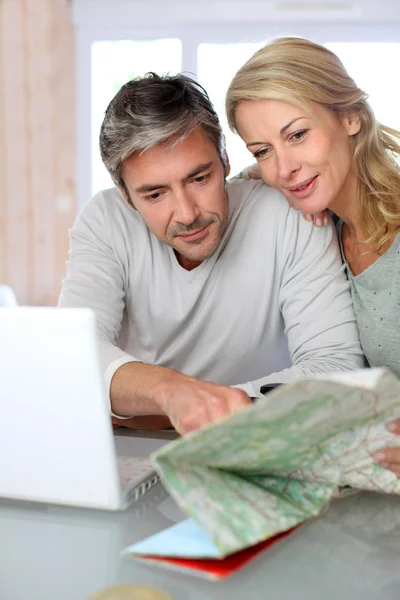 Mature couple planning vacation trip with map and laptop