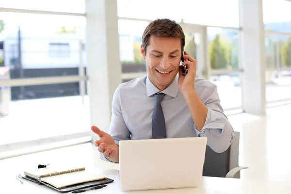 Happy businessman on the phone in front of laptop