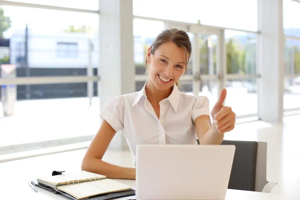 Cheerful office-worker showing thumbs up in front of laptop
