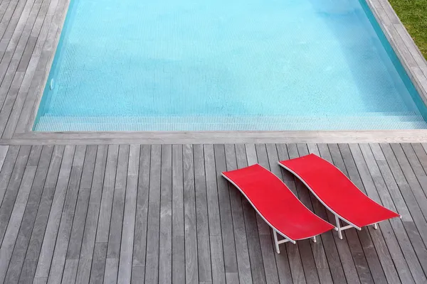 View of red long chairs set by swimming-pool