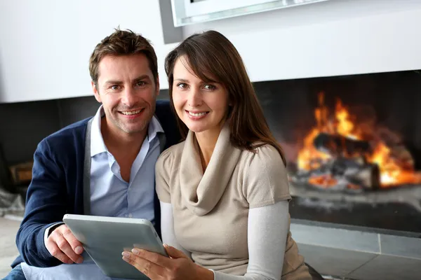 Couple sitting by fireplace and websurfing with tablet