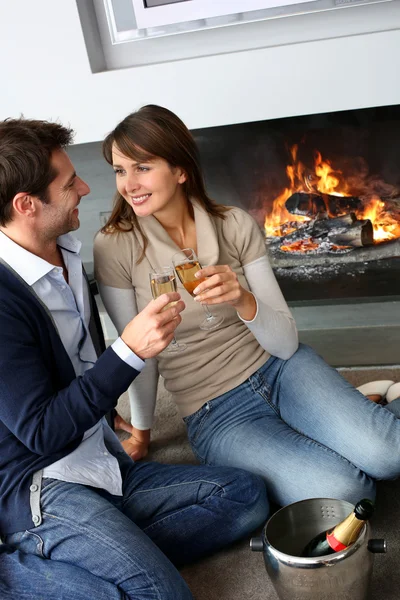 Cheerful couple drinking champaign by fireplace