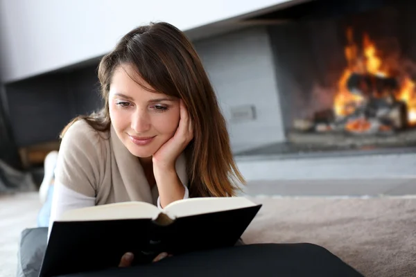 Portrait of beautiful woman reading book by fireplace