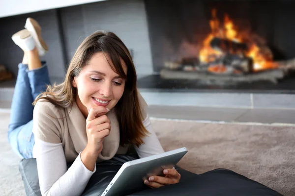 Woman using digital tablet laying by fireplace