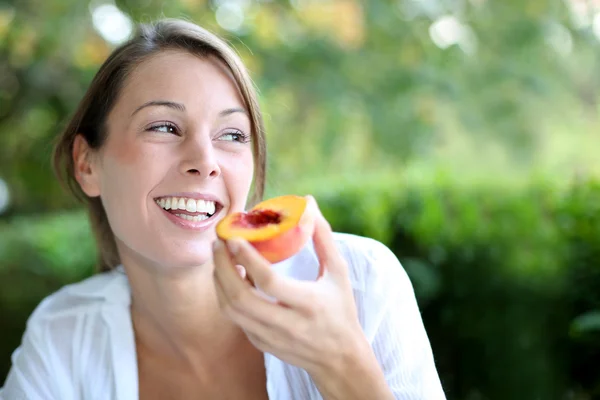 Smiling woman eating peach for breakfast