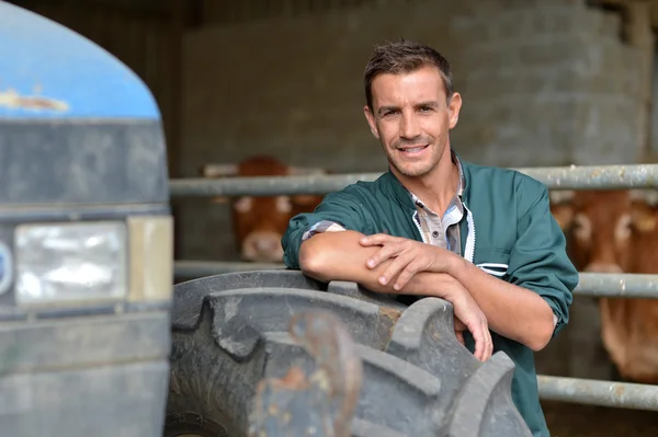 Handsome farmer leaning in barn on tractor wheel