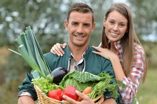 Portrait of couple of farmers holding basket of vegetables