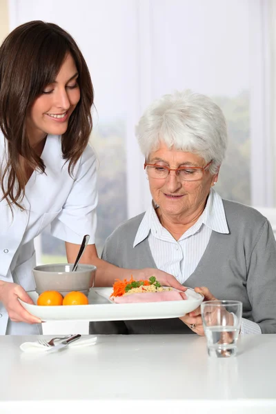 Beautiful nurse bringing meal tray to old woman at nursing home