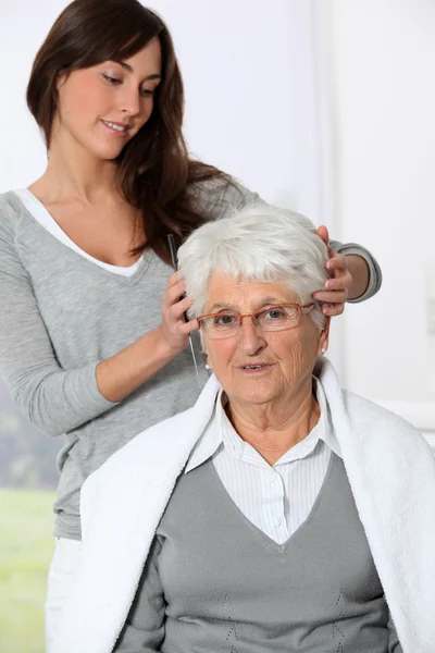 Young woman doing an haircut to old woman