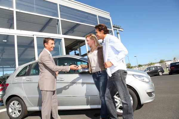 Car seller with couple outside car dealership