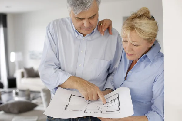 Senior couple at home looking at blueprint
