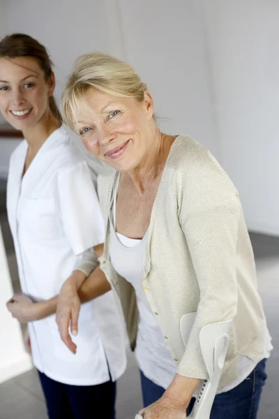 Nurse helping old woman to walk with crutches