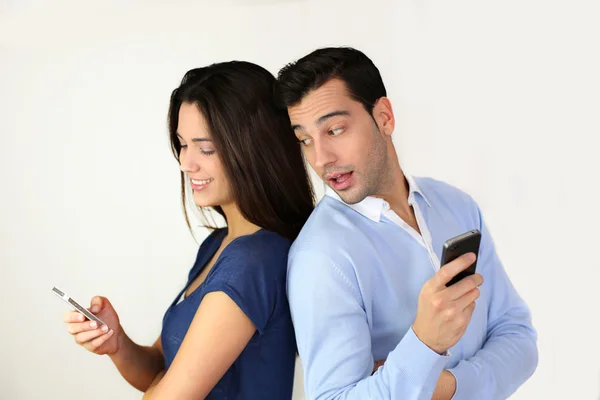 Couple standing back to back and using smartphone