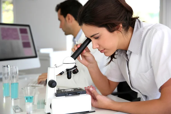 Young woman looking through microscope lense