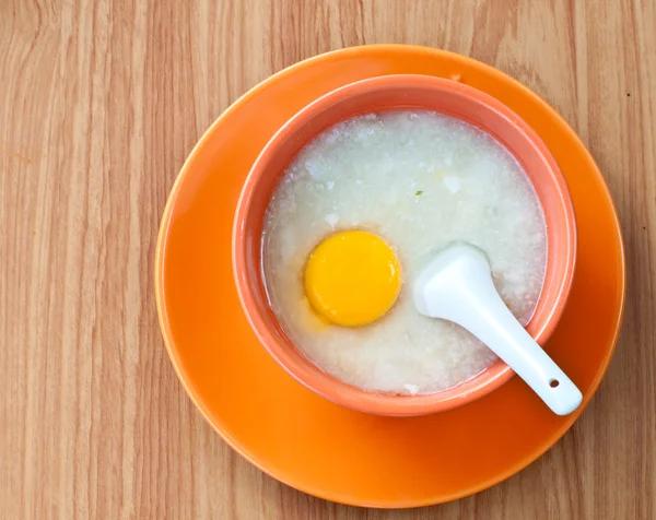 Rice porridge with egg in orange bowl.