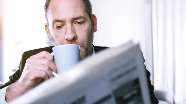 Businessman reading newspapers and drinking coffee