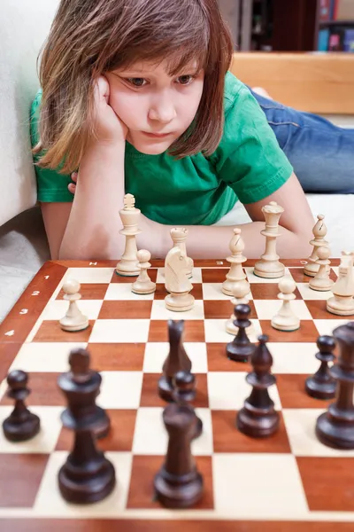 Little girl playing chess lying on couch